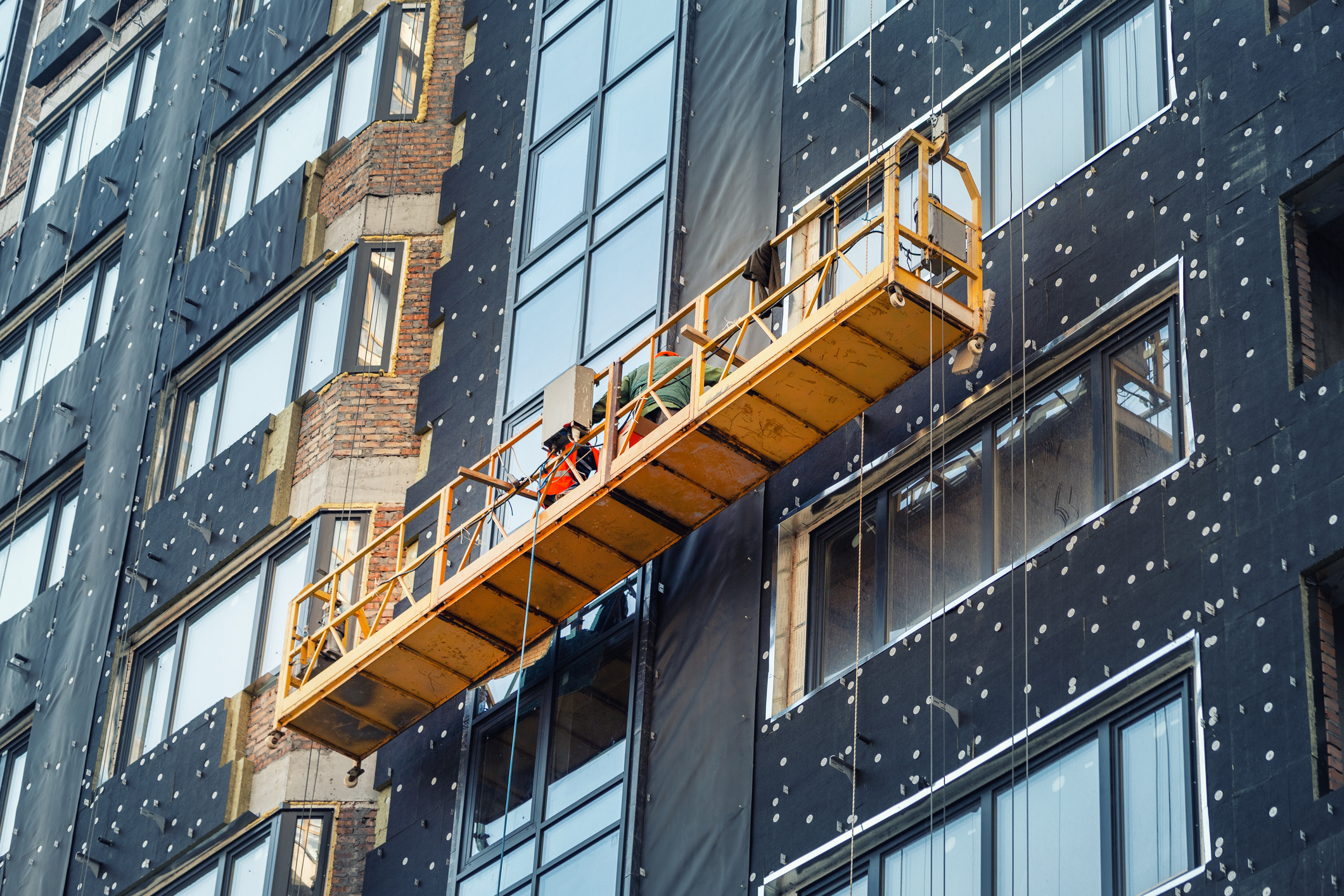 Suspended construction craddle near wall of hightower residentaial building with insulation and ventilated facade on construction site. Engineering urban background